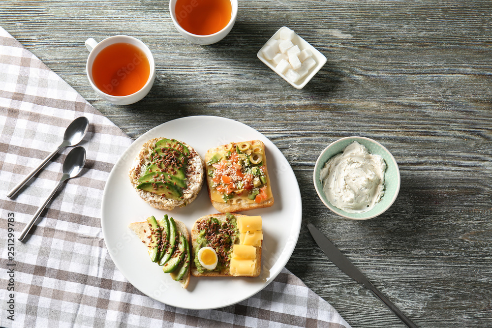 Plate with different tasty sandwiches and tea on wooden table