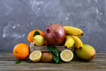Wall Mural - A pile of exotic fruits (bananas, oranges, kiwi, pomegranate, mango, guava, lemon) in a wooden box on the table.