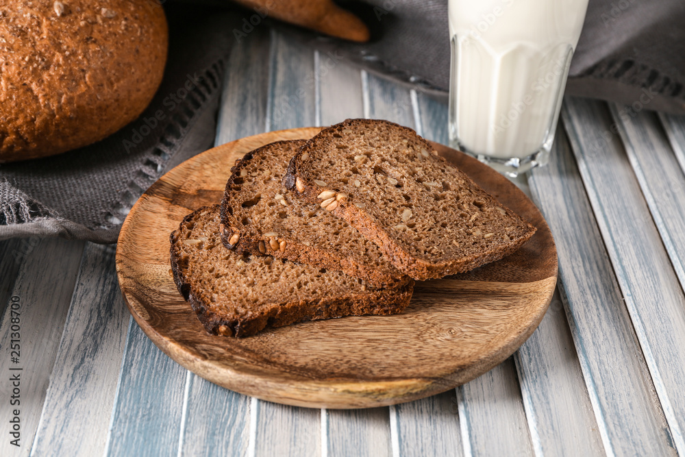 Wooden plate with slices on tasty fresh bread on table