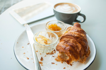 Fresh croissant with jam and butter and cappuccino with beautiful latte art on grey table in a cafe.