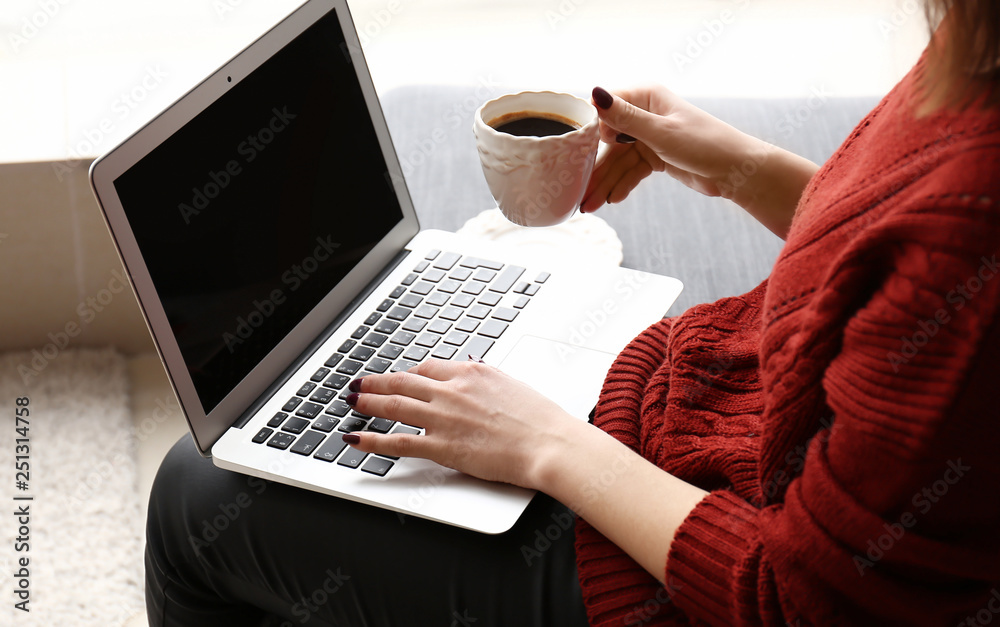 Young woman working on laptop and drinking coffee at home