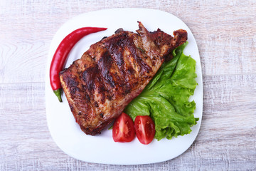 Pork ribs on barbeque and chili pepper with tomato, lettuce leaves on white plate