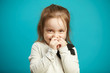 © Ilshat - Little shy girl smiles and covers her mouth with hands, expresses embarrassment and indecision, emotional photo of children shyness on blue background.