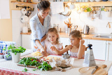 Family Are Cooking Italian Pizza Together In Cozy Home Kitchen. Cute Kids With Happy Mother Are Preparing Food Or Meal For Dinner. Two Girls Are Helping Woman. Children Chef Concept.