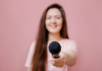 young woman with microphone in hand on pink background extends hand to camera