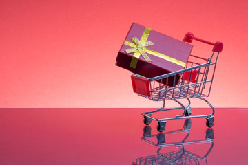 Shopping cart and gift box on red background, business and celebration concept. Selective focus