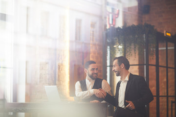 Wall Mural - Portrait of two smiling business people shaking hands after successful meeting shot from behind glass, copy space