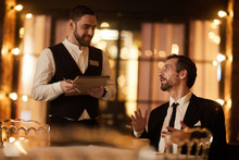 Portrait Of Mature Gentleman Ordering Food In Luxury Restaurant With Smiling Waiter Looking At Him, Copy Space