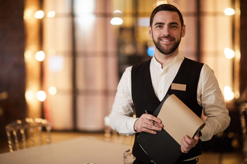 Waist up portrait of handsome waiter smiling cheerfully at camera standing in luxury restaurant or cafe, copy space