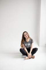 Portrait of a smiling young girl sitting with legs crossed isolated on white background. happy young  girl in torn jeans and gray t-shirt isolated on white