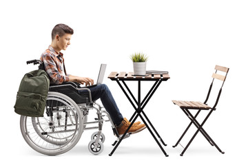 Canvas Print - Disabled teenage male student working on a laptop in a wheelchair and sitting alone in a cafe