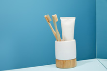Holder With Bamboo Toothbrushes, Toothpaste In Tube And Mirror On Table And Blue Background