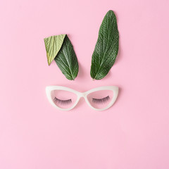 Happy Easter minimal concept. Bunny rabbit face made of natural green leaves with glasses on pastel pink background. Flat lay.