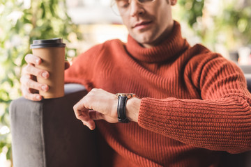 Sticker - selective focus of pensive man holding paper cup while looking at watch in cafe