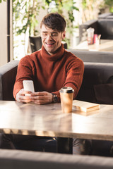 Sticker - smiling man using smartphone near disposable cup and book in cafe