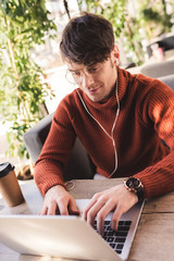 Sticker - cheerful man listening music in earphones while using laptop in cafe