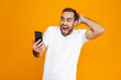 © Drobot Dean - Photo of optimistic man 30s in casual wear smiling and holding smartphone, isolated over yellow background