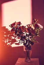 A Bouquet Of Roses In A Glass Vase Stand On A Wooden Stool Against The Background Of The Wall In The Rays Of Sunlight