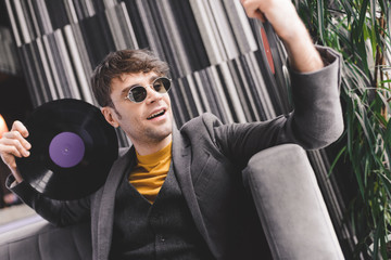 happy young man in sunglasses looking at vintage vinyl record