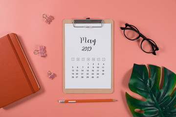 Flat lay calendar with clipboard, palm leaves and pencil on living coral color background. May 2019. top view.