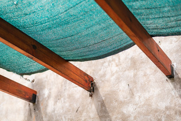A plastic sun protection mesh on wooden beams and a cracked concrete wall