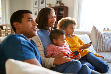 Wall Mural - Young family sitting together on the sofa in their living room watching TV, selective focus