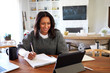 © Monkey Business - Smiling middle aged mixed race woman sitting at the table in her dining room looking at tablet computer and making notes, selective focus