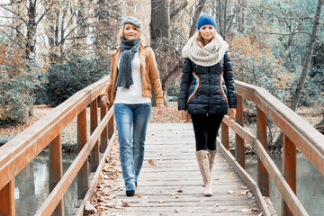 Two attractive young women posing on a wooden bridge