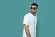 © Davidovici - Image of serious and confident young handsome man in white tshirt and sunglasses looking away, isolated over blue background.