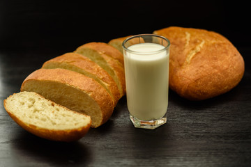 Ciabatta and a glass of milk on a wooden background.