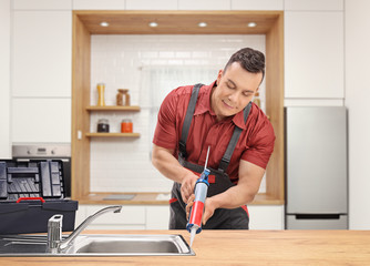 Poster - Plumber using a silicone tube on a sink inside a modern kitchen