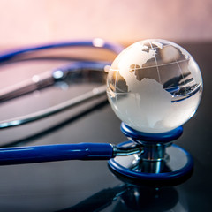 Global healthcare concept. World globe crystal glass on blue stethoscope on glossy desk. Health and medical science. Worldwide wellness business