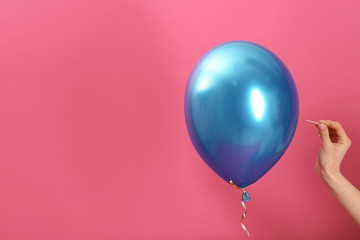 Woman piercing balloon with needle on color background, closeup. Space for text