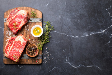 Wall Mural - Raw Fresh Marbled Meat Beef Steak rosemary, spices  and vintage ax  on a wooden board. Black marble background. Top View Copy space for Text