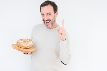 Senior man holding homemade fresh bread over isolated background surprised with an idea or question pointing finger with happy face, number one