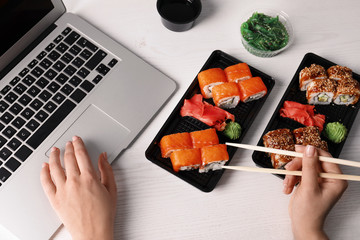 Woman eating tasty sushi rolls at workplace, closeup. Food delivery