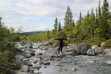 White Caucasian male tourist in sportswear stands in the middle of a mountain river with stones spread his arms