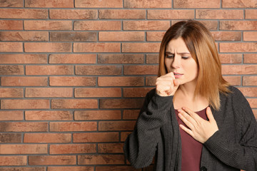 Wall Mural - Woman suffering from cough near brick wall. Space for text