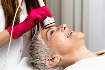 Wall Mural - Beautiful senior woman having radio waves lifting face treatment.