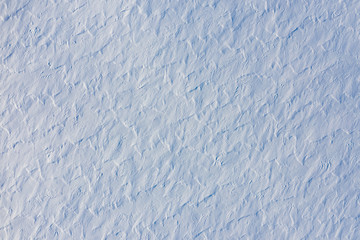 Snow covered land texture with grunge surface created by windy weather. Abstract winter backdrop in blue tones, top view from drone