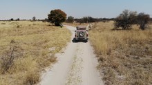 4x4 Offroad Vehicle Driving Through Wild Savannah Landscape Of Central Botswana Kalahari Landscape Close To Makgadikgadi Pans On The Way To Kubu Island, Aerial Drone Shot