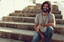 Handsome Stylish Man Wear Gray Shirt And Jewelries Sitting And Smiling On Old Stairs And Posing In Outdoor - Image