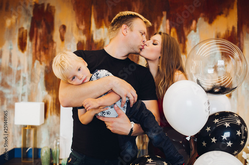 Adorable Husband And Wife Kissing While Man Holding Son In Hands