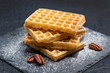 Sweet tasty Belgian waffles close-up, sprinkled with powdered sugar, pecan nuts