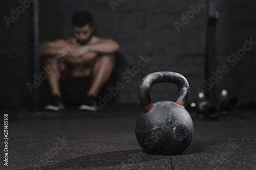 Sporty man sitting at the gym suffering breakdown to overcome. Demotivation sport concept. Stress and fatigue in sport. Crossfit kettlebell training.