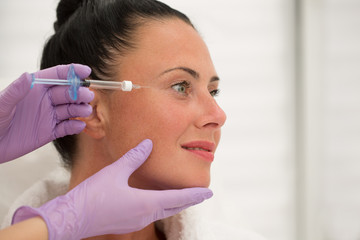 Closeup of woman face getting rejuvenation injection in beauty salon. Hands of doctor cosmetologist keeping syringe with hyaluronic acid and doing shot in skin around eyes. Concept of lifting.