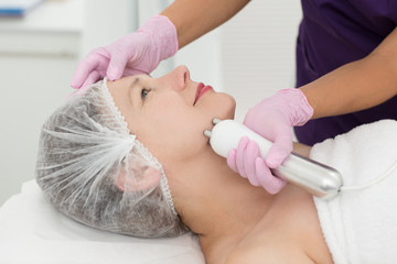 Wall Mural - Closeup of satisfied female client lying on couch and enjoying cosmetic therapy in cosmetology office. Smiling woman relaxing during facelifting. Concept of skin care and cosmetology.