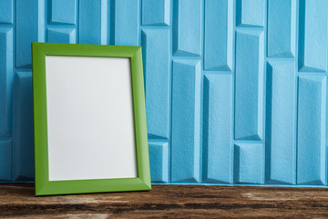 Green photo frame on old wooden table over blue wallpaper background