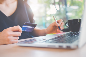 Wall Mural - Business woman's hand holds a credit card and uses a laptop computer to shop online.