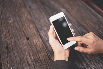 Woman hand using smart phone on old wood table texture background at coffee shop.